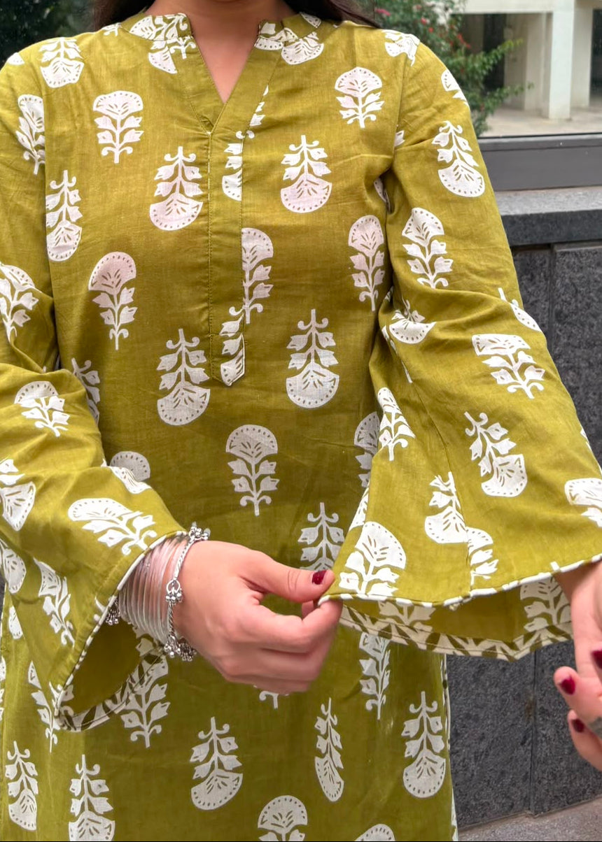 A woman wearing a mustard yellow kurta with a white block print pattern, featuring bell sleeves and a split neckline.
