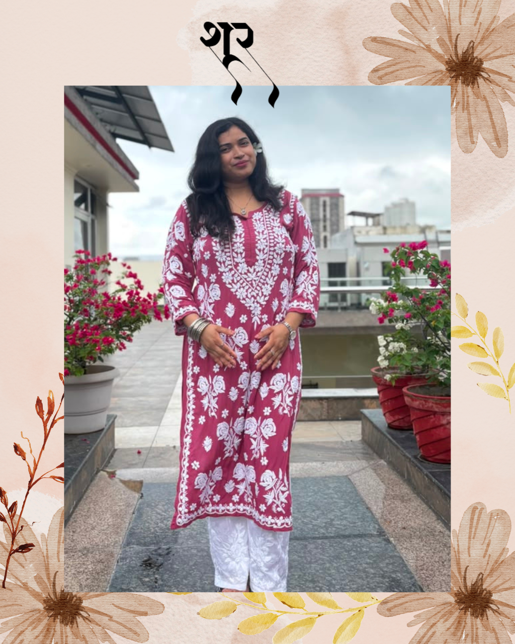 A woman stands on a rooftop terrace wearing a maroon pink and white printed kurta with white pants. The photo is framed with a decorative beige border featuring floral illustrations and a black symbol at the top.